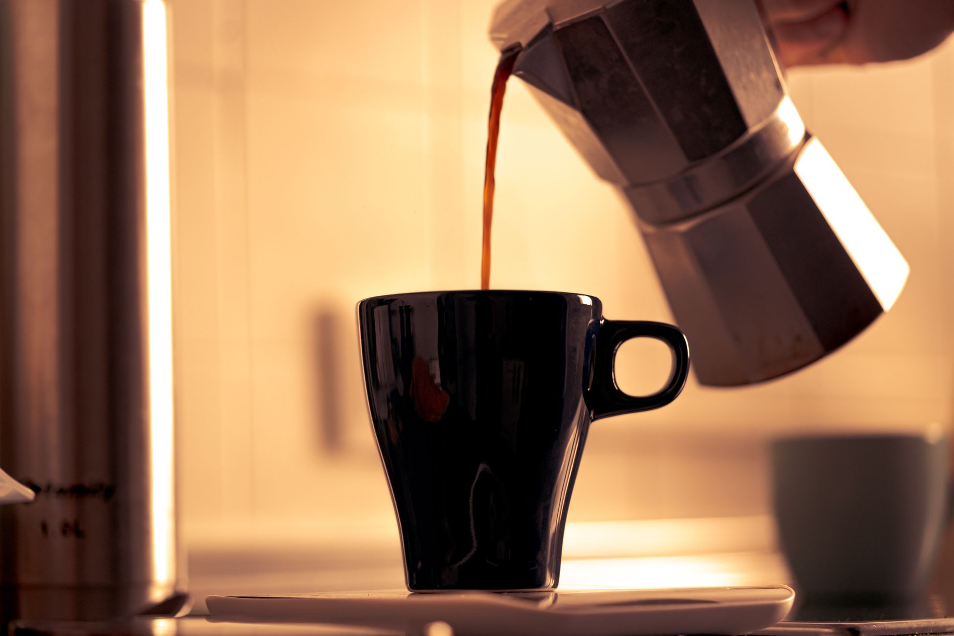 Warm morning coffee being poured into a cup from a classic moka pot.
